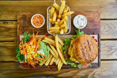 Burger mit Pommes und Salat angerichtet auf einer hölzernen Platte